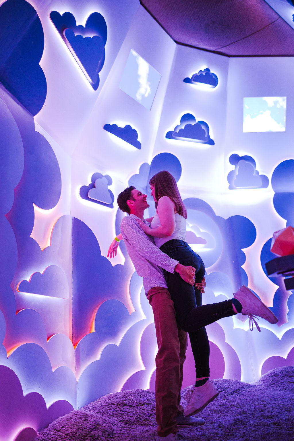 Justin lifts Liz against a background of white abstract highlights and shapes.